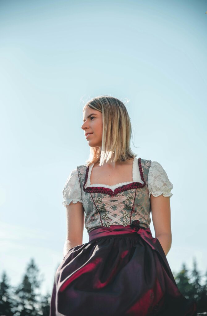 Blonde woman in traditional dirndl dress enjoying sunlight in Kitzbühel, Austria.